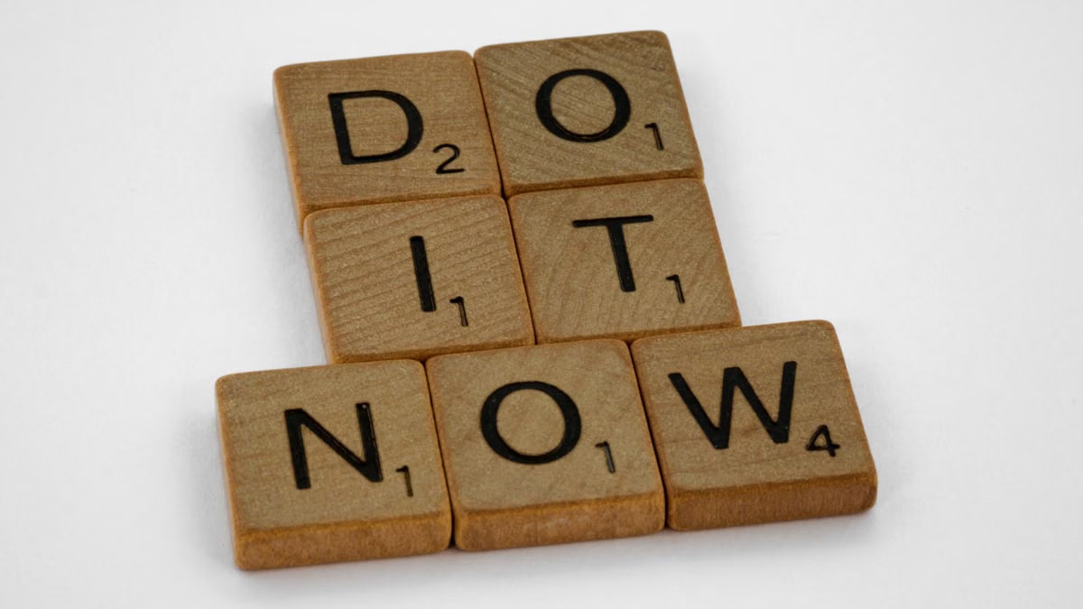 Wooden scrabble tiles forming 'DO IT NOW' on a minimal white backdrop. Inspiring concept.